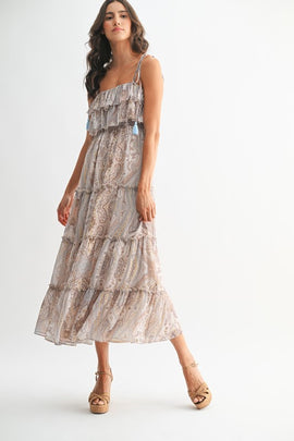 Woman wearing bohemian paisley maxi dress with ruffled neckline, tassel straps, and tiered flowy skirt.