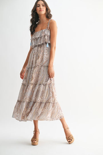 Woman wearing bohemian paisley maxi dress with ruffled neckline, tassel straps, and tiered flowy skirt.