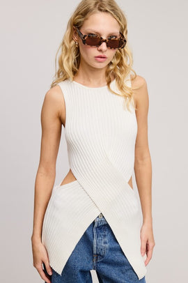 A sleeveless ribbed-knit sweater top with a criss-cross waist wrap design and side cut-outs, worn by a model with sunglasses and a jean skirt.