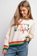 Woman wearing a sweater with 'Merry & Bright' text and rainbow colors on a plain background