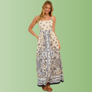 Front view of person wearing a cream maxi dress with blue floral border print, straight neckline, and flowy maxi skirt.