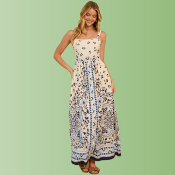 Front view of person wearing a cream maxi dress with blue floral border print, straight neckline, and flowy maxi skirt.