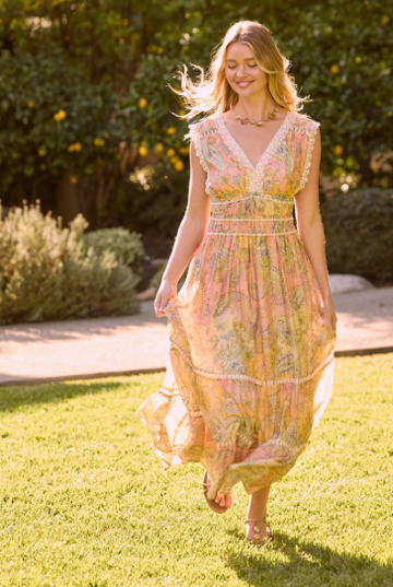 Person walking on grass wearing a pastel paisley print tiered maxi dress with lace trim, V-neckline, cap sleeves, and a defined waist.