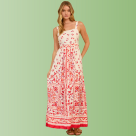 Front view of person wearing a cream maxi dress with red floral border print, straight neckline, and flowy maxi skirt.