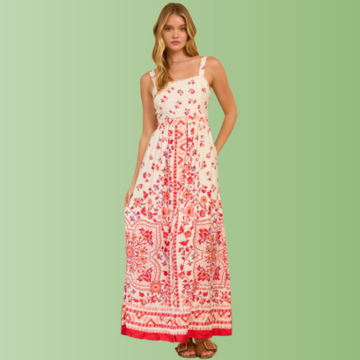 Front view of person wearing a cream maxi dress with red floral border print, straight neckline, and flowy maxi skirt.