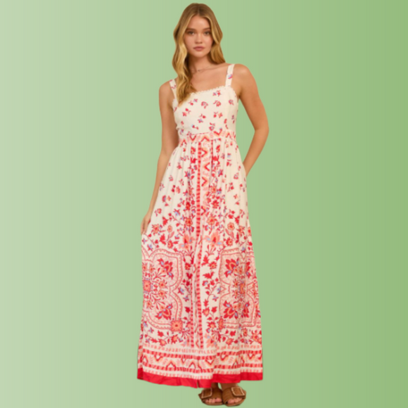 Front view of person wearing a cream maxi dress with red floral border print, straight neckline, and flowy maxi skirt.