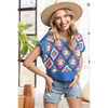 A woman wearing a multi-color crochet vest top with short sleeves, paired with denim shorts and a wide-brimmed hat.