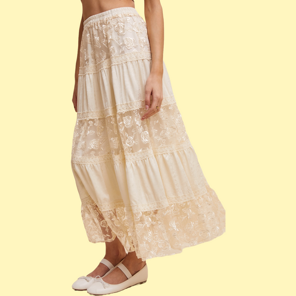 A floral embroidered tiered maxi skirt in beige, with a woman standing and showing the skirt's length and fit.