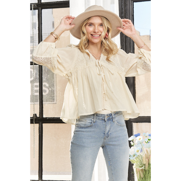 A woman wearing a beige long sleeve knit peasant blouse with puff sleeves, paired with blue jeans and a wide-brimmed hat.