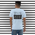 Light Blue Short Sleeve T-Shirt. The word "TOOL" written across shoulders with the "O's" replaced with outline of peaches. The word sits on top of a black box with the word "SHED" done in a white outline written in the box.